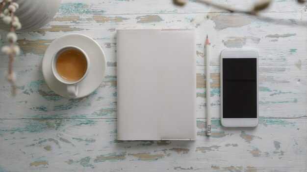 Vista superior del lugar de trabajo rústico con teléfono inteligente, papelería y taza de café