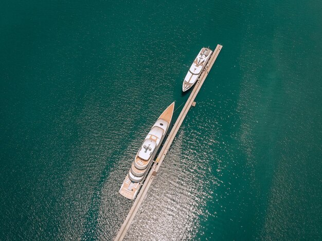 Vista superior de los lujosos yates blancos amarrados en el muelle largo y delgado, mar azul en un día soleado; concepto millonario.