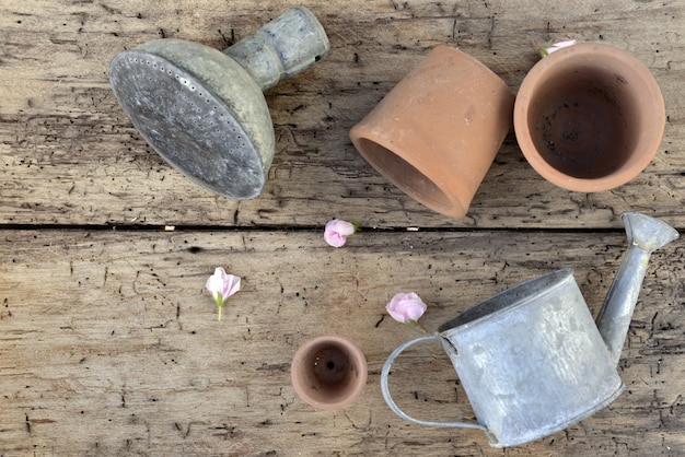 Vista superior de macetas de terracota y una pequeña regadera en una tabla rústica con pétalos