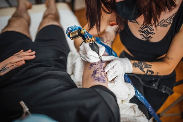 Foto vista superior de un maestro de tatuaje femenino tatuando el brazo de un hombre en un estudio