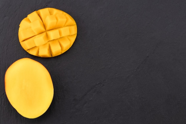Vista superior del mango maduro cortado por la mitad y cortado en cubitos sobre pizarra oscura.