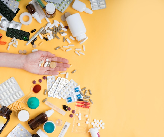 Vista superior de la mano femenina sosteniendo píldoras de tabletas contra el fondo amarillo Muchas tabletas, píldoras, medicamentos y otros accesorios médicos