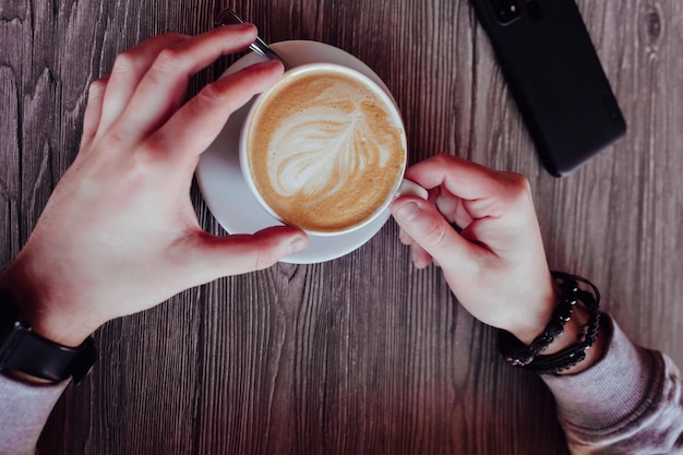 Vista superior de la mano de un hombre bebiendo café en una mesa. taza de capuchino con espuma