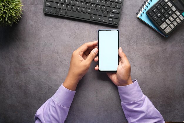 Vista superior de la mano del hombre que sostiene el teléfono inteligente con pantalla vacía en el escritorio de oficina