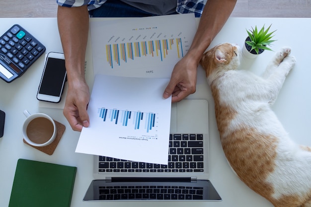 Una vista superior de la mano de un hombre sobre un escritorio escribe un gráfico de pérdidas y ganancias en la computadora portátil en casa. Trabajo autónomo a domicilio. Trabajar desde el concepto de casa