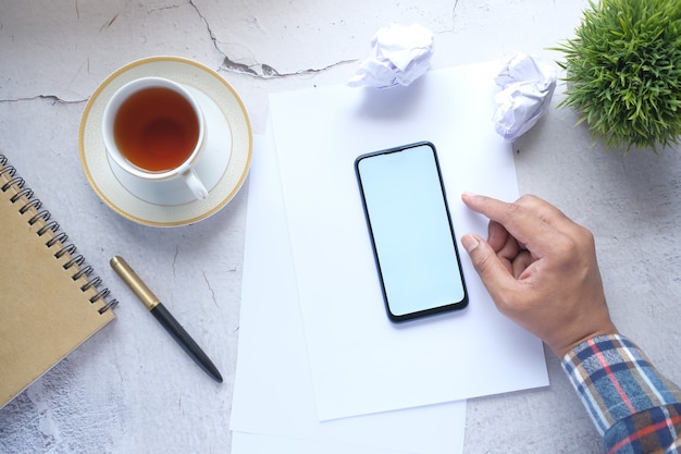 Vista superior de la mano del hombre con teléfono inteligente en el escritorio de oficina