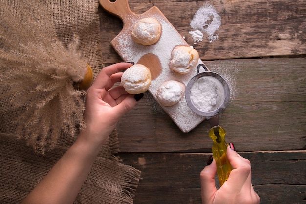 Vista superior de la mano de mujer decorando con azúcar glas algunos profiteroles. Estilo rústico