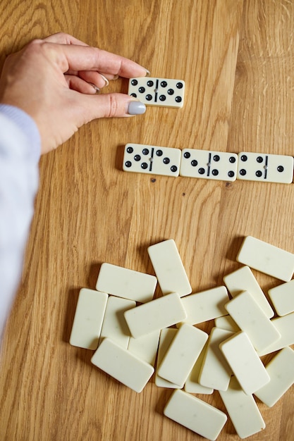 Vista superior de la mano de la mujer jugar juegos de dominó blanco sobre fondo de mesa de madera con concepto de juego de mesa de espacio de copia