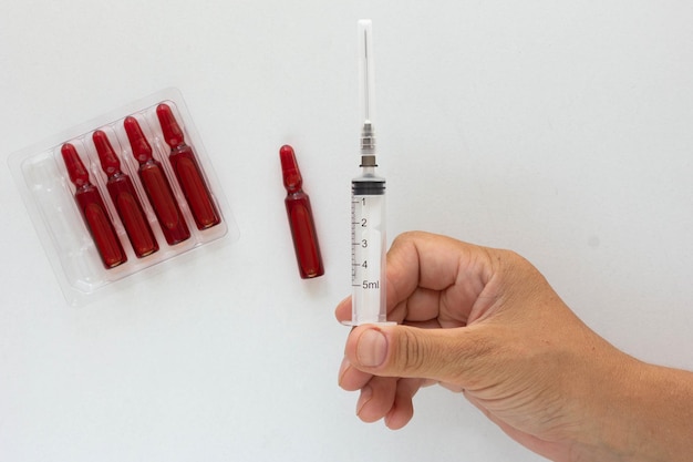 Vista superior de la mano de la mujer que sostiene la inyección para ampolla con vitaminas del grupo B en el fondo blanco