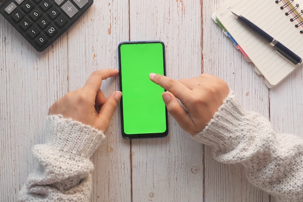 Vista superior de la mano de las mujeres sosteniendo el teléfono inteligente en la mesa