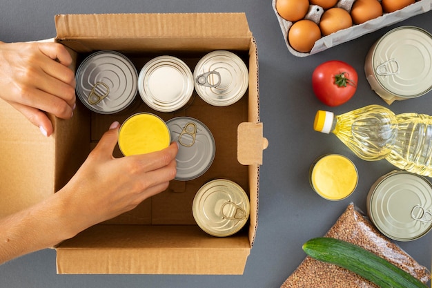 Vista superior de la mano preparando donaciones de alimentos en caja