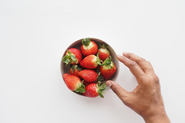 Vista superior de la mano que busca fresas en un recipiente sobre la mesa