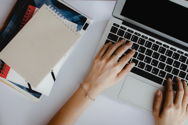 Vista superior de la mano usando la computadora portátil con una pila de libros en el escritorio de oficina blanco para el aprendizaje electrónico, el trabajo en casa y el concepto de espacio de trabajo