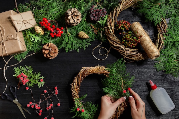 Vista superior de las manos femeninas hacen una corona de navidad llena de regalos y pergaminos ramas de abeto y herramientas ...