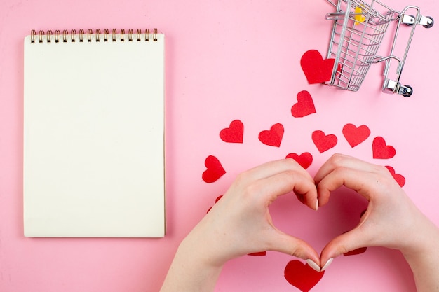 Vista superior de las manos femeninas haciendo el signo del corazón pegatinas de corazón rojo mini carro portátil en la mesa azul