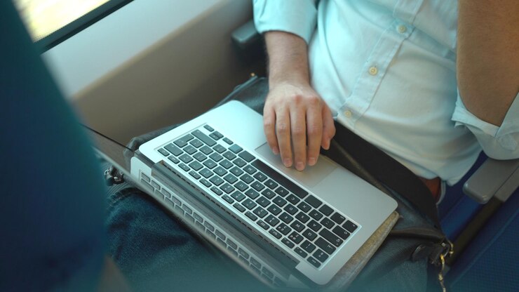 Vista superior de las manos de un hombre de negocios irreconocible usando su computadora portátil mientras viaja en un tren