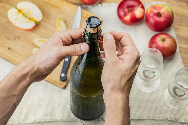 Vista superior de las manos masculinas abriendo la botella de cidre premium. Disparo desde arriba de descorchar hermosa botella helada de vino de manzana