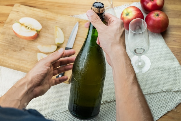 Vista superior de manos masculinas que sostienen la botella tapada con corcho de cidre premium. Tomada desde arriba con una hermosa botella helada de vino de manzana en manos del hombre