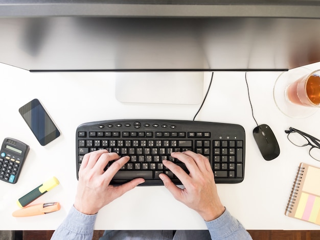 Vista superior de las manos masculinas que trabajan en la computadora en el escritorio.