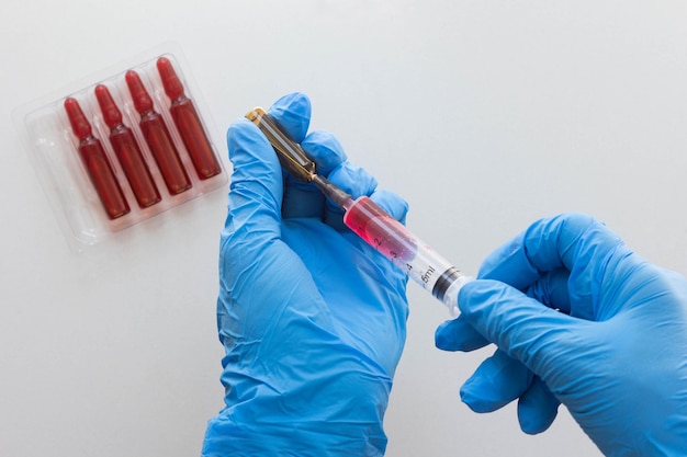 Vista superior de las manos de la mujer en guantes médicos llenando el cilindro de la jeringa con vitamina del grupo B para inyección sobre fondo blanco