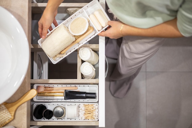 Foto vista superior de las manos de la mujer organizando cuidadosamente las comodidades del baño y los artículos de tocador en el cajón del baño