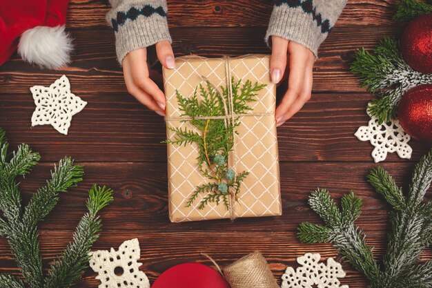 Vista superior de las manos de una mujer con un regalo de Navidad sobre fondo de madera