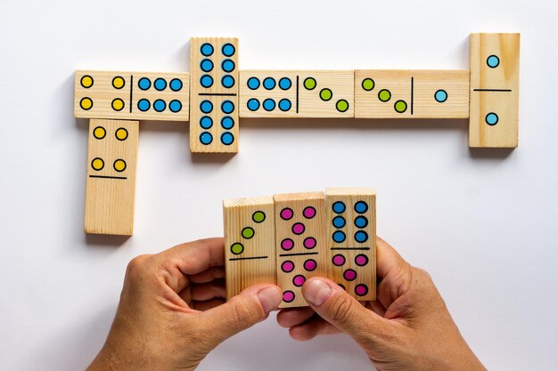 Vista superior de manos de mujer sosteniendo piezas de juego de dominó de madera sobre el fondo blanco