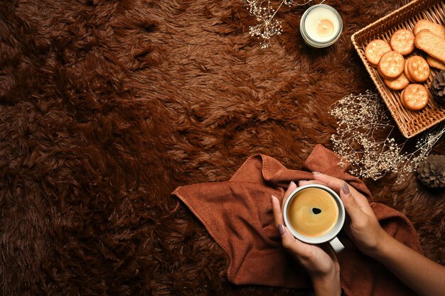 Vista superior de manos de mujer sosteniendo una taza de café en la alfombra marrón