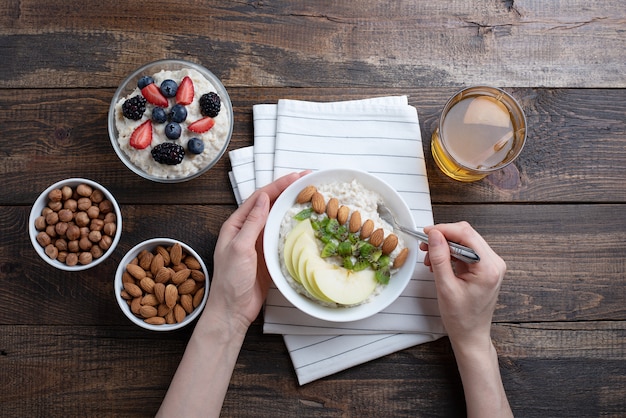 Vista superior de las manos de las mujeres en el desayuno, avena con almendras y manzana, nueces, bayas, compota.