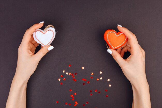 La vista superior de las manos de la niña sostiene corazones rojos y blancos. alrededor de dulces de corazones rojos. Fondo gris. Día de San Valentín.