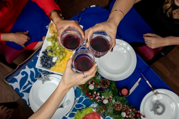 Vista superior de las manos con vasos brindando en una cena de Navidad con decoración navideña en la parte posterior
