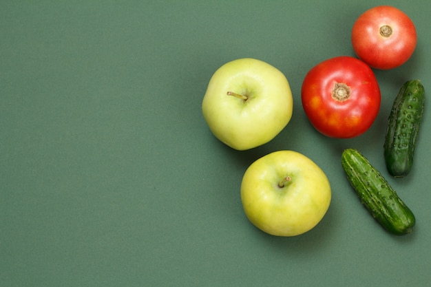 Vista superior de manzanas frescas, tomates y pepinos sobre fondo verde. Verduras y frutas en la mesa de la cocina.