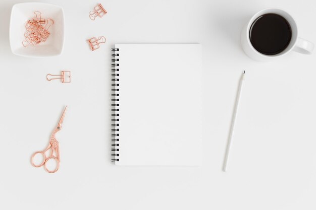 Vista superior de una maqueta de cuaderno blanco con accesorios de espacio de trabajo y una planta suculenta sobre una mesa blanca