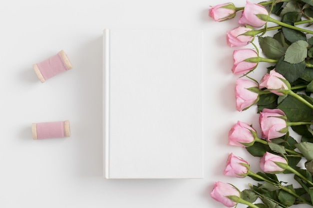 Vista superior de una maqueta de libro con rosas rosadas sobre una mesa blanca