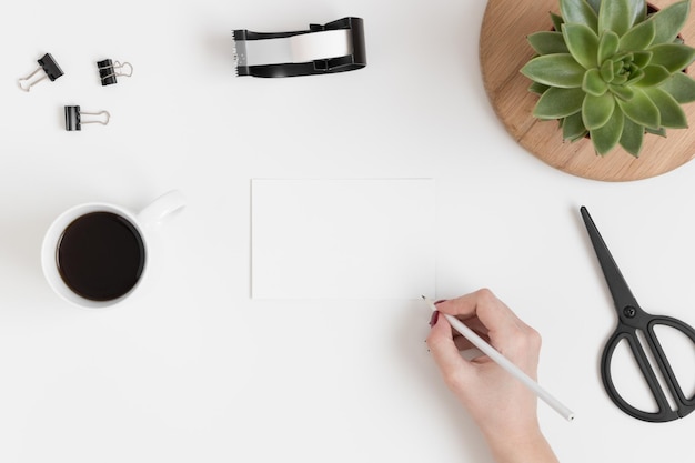 Foto vista superior de una maqueta de tarjeta blanca con accesorios de espacio de trabajo y una planta suculenta sobre una mesa blanca