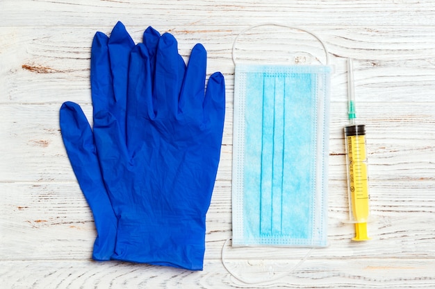 Vista superior de la mascarilla quirúrgica desechable, un par de guantes médicos de látex y una jeringa sobre fondo de madera. Proteja su concepto de salud con espacio de copia.