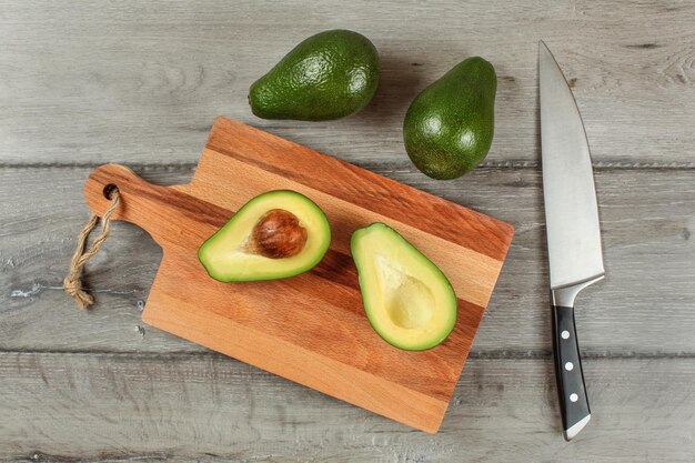 Vista superior de la mesa: aguacate cortado por la mitad en una tabla de cortar de madera, cuchillo de chef al lado, dos peras verdes enteras arriba.