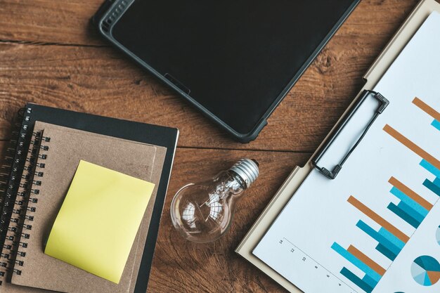 La vista superior de una mesa de madera es un escritorio en la oficina de una empresa nueva en la mesa hay una bombilla, una tableta, cuadernos y documentos financieros Espacio de copia de vista superior plana