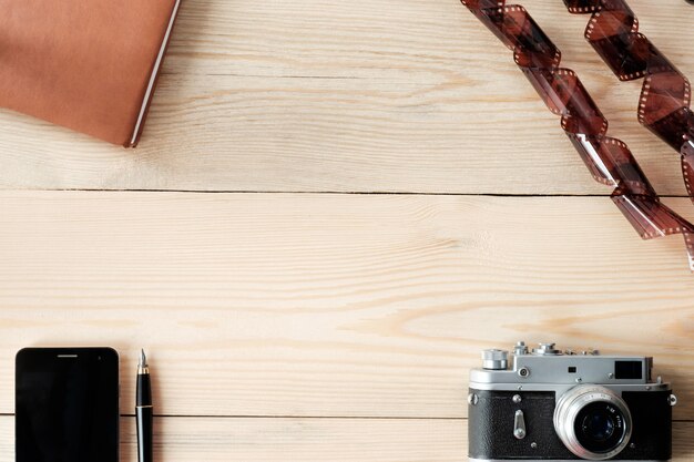 Vista superior de la mesa de madera con teléfono; bolígrafo, diario, cámara vintage y película