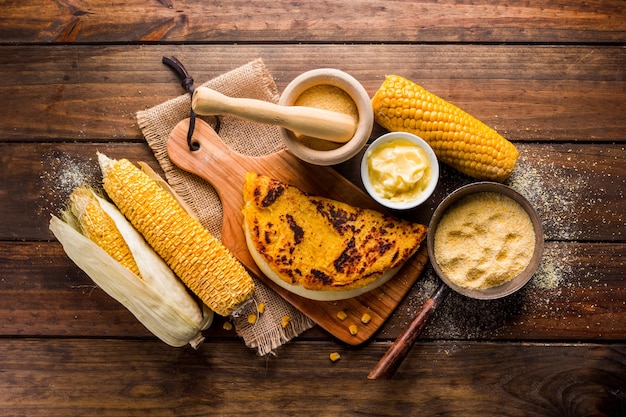 Vista superior de una mesa de madera con varios ingredientes para la preparación de Cachapas con queso