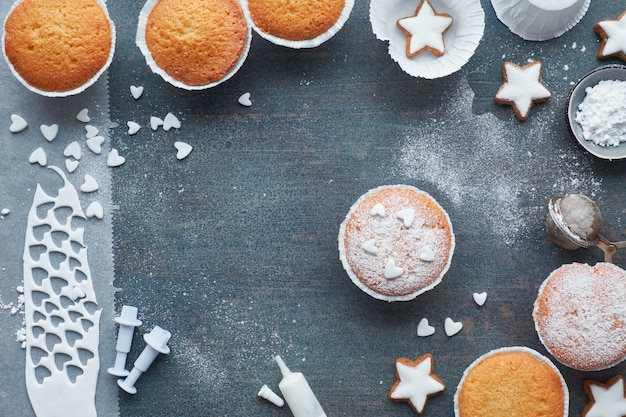 Vista superior de la mesa con muffins espolvoreados de azúcar, glaseado de fondant y galletas de estrella de Navidad en madera azul