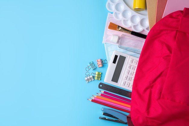 Foto vista superior de la mochila rosa con material escolar sobre fondo de mesa azul, concepto de diseño de regreso a la escuela.