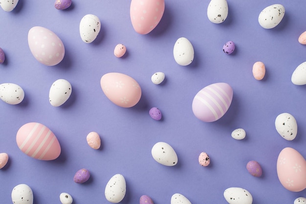 Vista superior de un montón de huevos de Pascua multicolores de diferentes tamaños con rayas y puntos en el fondo violeta pastel aislado