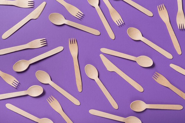 Vista superior de muchas cucharas y tenedores de bambú sobre fondo violeta, copie el espacio. Concepto de ropa de mesa desechable para llevar