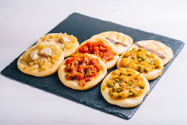 Vista superior de muchas mini pizzas recién horneadas. Repostería tradicional española con verduras.