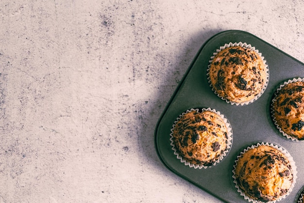 Vista superior de muffins con chispas de chocolate en placa de horno sobre fondo blanco.