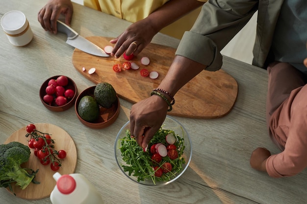 Vista superior de la mujer cortando verduras a bordo para la ensalada con su marido ayudándola