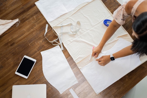 Vista superior de la mujer costurera moderna que trabaja con patrones de costura en la mesa en el taller de confección