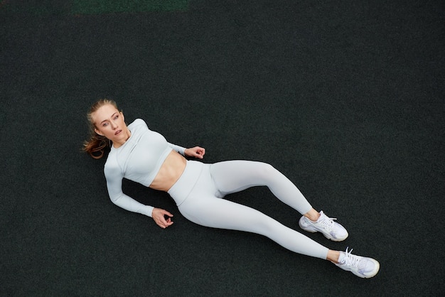 Vista superior de una mujer feliz sentada en la carretera después de correr por la mañana Mujer en forma en la carretera tomando un descanso después de hacer ejercicio al aire libre