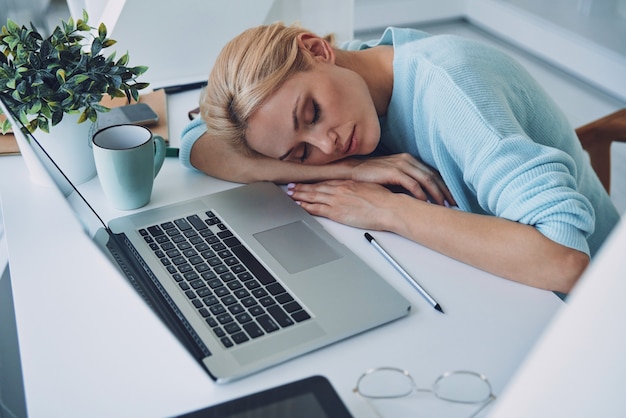 Vista superior de la mujer joven cansada durmiendo mientras está sentada en su lugar de trabajo en la oficina